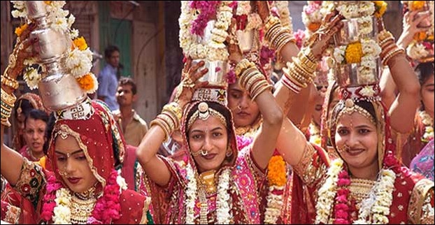 Rajasthani women with brightest fineries color their hands and feet with mehendi and carry Ghudilas on their head