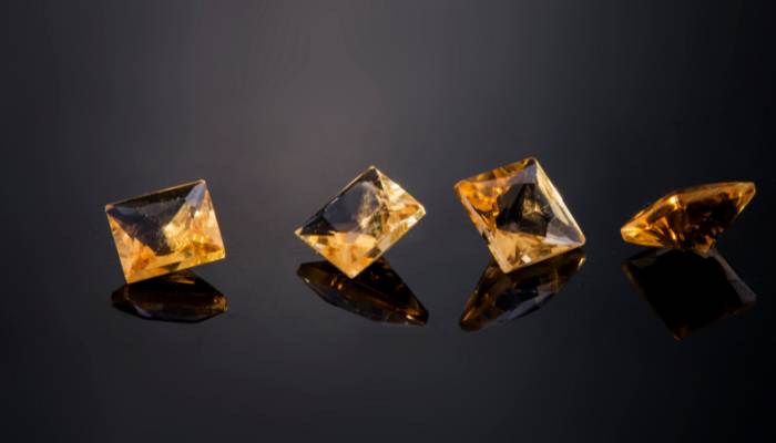Image of a yellow citrine gemstone resting on a black background. 