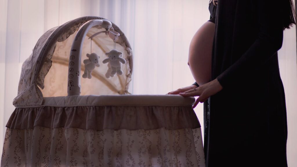 Image shows a pregnant woman watching baby cradle